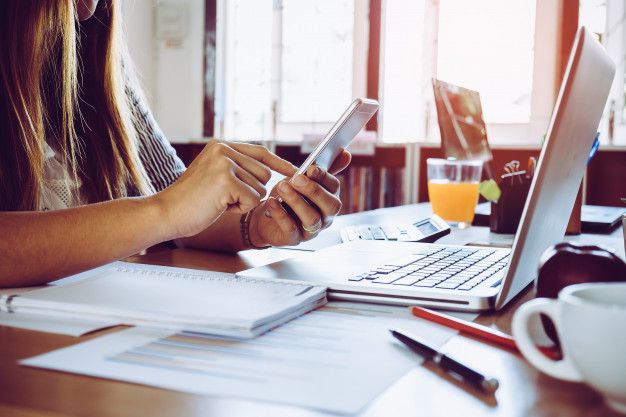 close-up-of-a-woman-hand-using-a-smart-phone-with-laptop-on-a-desk-at-office_2379-451.jpg